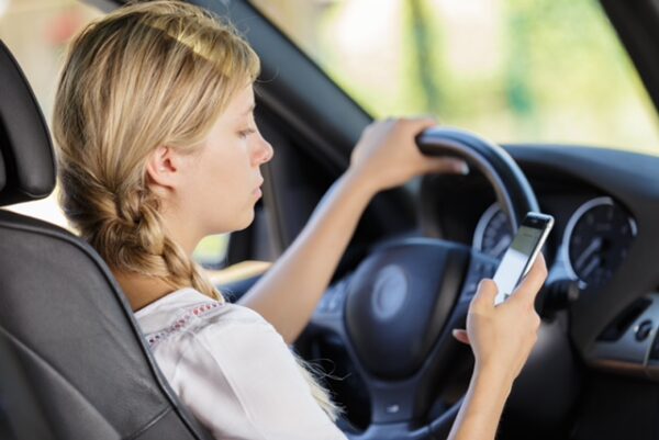 Distracted teen driver looks at cellphone while driving.