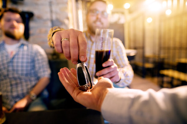 A man under the influence of alcohol hands over his car keys to a designated sober driver.