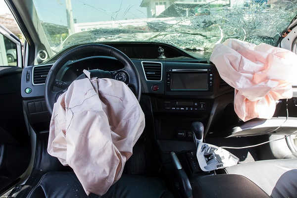 The inside of a vehicle following a serious car accident. Airbags are deployed and the windshield is smashed.