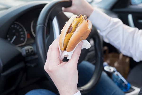 Man eating an hamburger while driving his car.